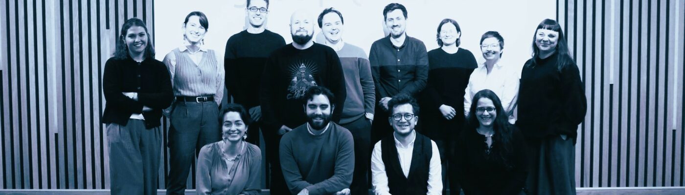 a group of smiling people stand and crouch in front of a presentation screen