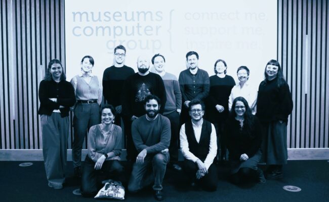 a group of smiling people stand and crouch in front of a presentation screen